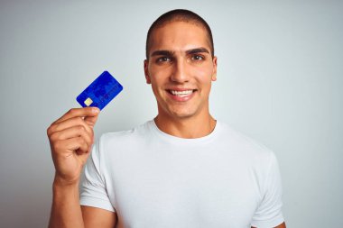 Genç yakışıklı adam ayakta mutlu bir yüz ile beyaz izole arka plan üzerinde kredi kartı tutan ve dişleri gösteren kendinden emin bir gülümseme ile gülümseyerek