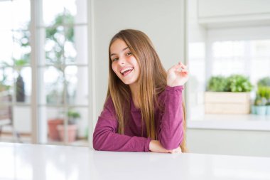 Beyaz masada güzel genç kız çocuk mutlu yüz zafer işareti yapıyor kamera göz kırpıyor ile gülümsüyor. İki numara.