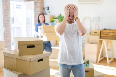 Genç çift karton kutular yeni bir eve hareket eden, evde baş ağrısı umutsuz ve stresli çünkü ağrı ve migreni vurguladı kel adam ayakta. Eller baş.