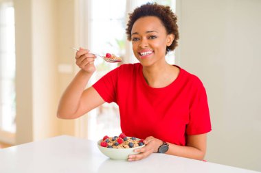 Sağlıklı kahvaltı sağlıklı kepekli tahıllar ve çilek yeme afro saçlı genç güzel bir Afrikalı-Amerikalı kadın