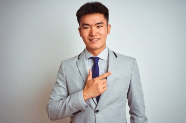 Çıplak beyaz arka plan üzerinde ayakta gri ceket ve kravat giyen Asya Çinli işadamı yüz üzerinde mutlu ve doğal ifade ile yan yukarı el ve parmak ile işaret eden bir gülümsemek ile neşeli