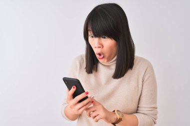 Genç güzel Çinli kadın bir sürpriz yüz ile şok korkuyor izole beyaz arka planda ayakta akıllı telefon kullanarak, korkuyor ve korku ifadesi ile heyecanlı