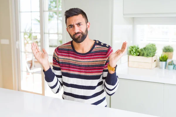 英俊的西班牙男子穿着条纹毛衣在家里无知和混乱的表情与手臂和手抬起 怀疑概念 — 图库照片