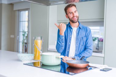 Yakışıklı adam mutfak yemek İtalyan spagetti makarna mutlu yüz görünümlü ve başparmak yukarı ile yan işaret ile gülümsüyor.