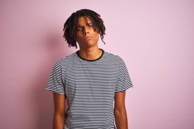 Koyu pembe arka plan üzerinde ayakta lacivert çizgili t-shirt giyen dreadlocks ile Afro adam şüpheci ve sinir, sorun nedeniyle üzgün çatık. Negatif kişi.