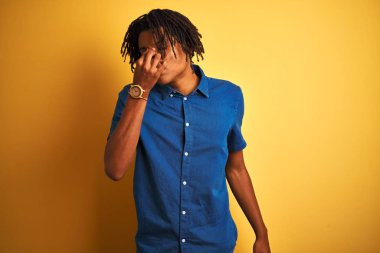 Sarı arka plan yorgun sürtünme burun ve gözleri hissi yorgunluk ve baş ağrısı üzerinde ayakta rahat denim gömlek giyen dreadlocks ile Afro adam. Stres ve hayal kırıklığı kavramı.