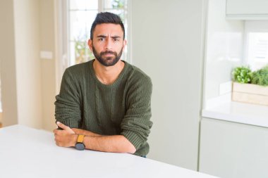 Yüz çapraz kolları olan ev kuşkucu, rahat kazak ve sinir, onaylamayan ifade giyen yakışıklı İspanyol adam. Negatif kişi.