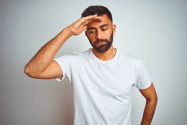 Young indian man wearing t-shirt standing over isolated white background worried and stressed about a problem with hand on forehead, nervous and anxious for crisis