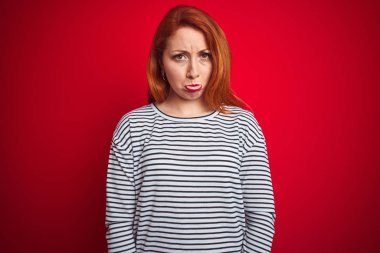 Genç kızıl saçlı kadın kayışlar lacivert gömlek kırmızı izole arka plan üzerinde ayakta depresif ve sıkıntı için endişe giyen, kızgın ve korkmuş ağlıyor. Hüzünlü ifade.