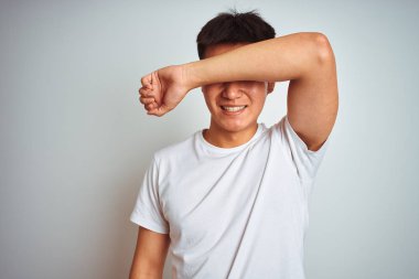 Genç Asyalı Çinli adam kol gülümseyen neşeli ve komik gözler ile izole beyaz arka plan üzerinde ayakta tişört giymiş. Kör kavram.