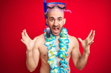İzole kırmızı arka plan üzerinde Dalış Şnorkel gözlük ve Hawaii Lei çiçekler giyen genç adam çılgın kutluyor ve başarı için hayran silah kaldırdı ve açık gözleri heyecanlı çığlık. Kazanan kavramı
