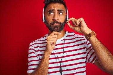 Genç Hint çağrı merkezi ajan adam üzerinde kulaklık kullanarak izole kırmızı arka plan ciddi yüz düşünme hakkında soru, çok karışık fikir