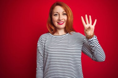 Genç Redhead kadın giyen strapes Lacivert gömlek ayakta kırmızı izole arka plan gösteren ve parmak sayısı dört ile işaret kadar güven ve mutlu gülümseyen.