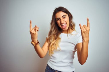 Genç güzel kadın izole arka plan üzerinde rahat beyaz t-shirt giyen çılgın ifade elleri ile kaya sembolü yapıyor bağırarak. Müzik yıldızı. Ağır müzik konsepti.