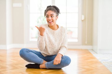 Seyir ve başparmak yanında yukarıyı mutlu yüz ile gülümseyen katta oturan afro saçlı güzel genç Afro-Amerikan kadın.