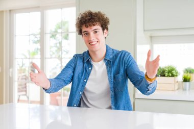 Evde rahat kot ceket giyen genç yakışıklı adam sarılmak için açık kollarla gülümseyerek kameraya bakıyor. Mutluluğu kucaklayan neşeli ifade.