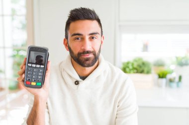 Akıllı yüz düşünme ciddi bir güven ifadesi ile satış terminali dataphone noktası tutan yakışıklı İspanyol adam