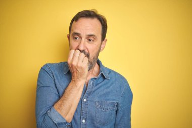 İzole sarı arka plan üzerinde gri saçlı yakışıklı orta yaş kıdemli adam vurguladı ve ağız ısırma tırnaklar elleri ile gergin bakıyor. Anksiyete sorunu.