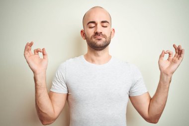İzole arka plan üzerinde rahat beyaz t-shirt giyen sakal ile genç kel adam Relax ve gözleri ile gülümseyen meditasyon jest parmaklar ile kapalı. Yoga konsepti.