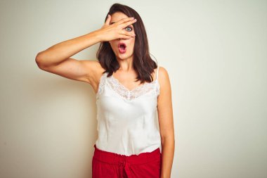 Beyaz izole arka plan üzerinde ayakta t-shirt giyen genç güzel kadın el ile yüz ve gözler kapsayan şokta göz atma, utanmış ifade ile parmaklar bakarak.