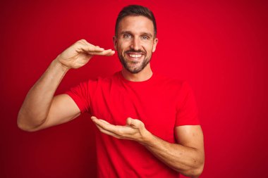 Kırmızı izole arka plan üzerinde rahat t-shirt giyen genç yakışıklı adam eller büyük ve büyük boyutlu işareti, ölçmek sembolü gösteren ile işaret. Kameraya bakarak gülümsüyor. Ölçme konsepti.
