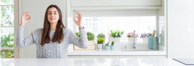 Evde beyaz masada oturan güzel genç kadının geniş açı resim rahatlayın ve gözleri ile gülümseyen meditasyon jest parmaklar ile kapalı. Yoga konsepti.