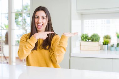 Sarı kazak giyen güzel genç kadın hayran ve kameraya gülümsüyor el ile sunmak ve parmak ile işaret ederken.