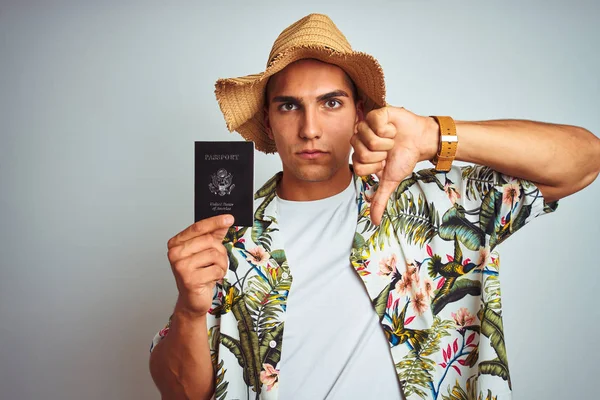 Young handsome man holding United States passport over white isolated background with angry face, negative sign showing dislike with thumbs down, rejection concept