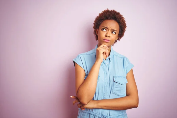 Young beautiful african american woman with afro hair over isolated pink background with hand on chin thinking about question, pensive expression. Smiling with thoughtful face. Doubt concept.
