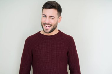 Genç yakışıklı adam izole arka plan üzerinde bir kazak giyen seksi ifade, neşeli ve mutlu yüz ile kameraya bakarak göz kırpma.