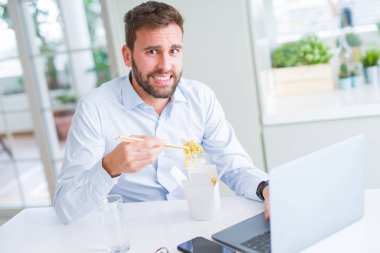 İş adamı yemek götürün Asya erişte yemek çalışma kullanırken bilgisayar dizüstü ve gülümseyen