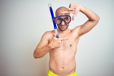 Genç adam dalış şnorkelli yüzme gözlük giyen izole arka plan üzerine teçhizat el ve parmaklar ile mutlu yüz ile kare yapma gülümseyen. Yaratıcılık ve Fotoğrafçılık konsepti.
