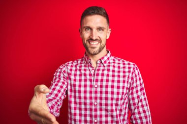 Kırmızı izole arka plan üzerinde genç yakışıklı adam tebrik ve karşılama gibi el sıkışması dostça gülümseyen. Başarılı iş.