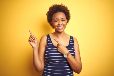 Beauitul Afrika Amerikan kadın izole sarı arka plan üzerinde yaz t-shirt giyiyor gülümseyen ve iki el ve parmak tarafına işaret kamera bakıyor.
