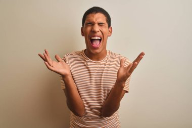 Genç yakışıklı Arap adam izole beyaz arka plan üzerinde çizgili t-shirt giyen kollarını kaldırdı ve kapalı gözleri heyecan çığlık ile başarı için deli ve deli kutluyor. Kazanan kavramı