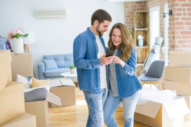 Genç çift karton kutular etrafında akıllı telefon kullanarak yeni bir eve hareket