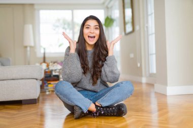 Evde katta oturan genç güzel kadın çılgın ve başarı için hayran kaldırdı Kollarını açarak kutluyor ve heyecanlı çığlık gözleri açık. Kazanan kavramı