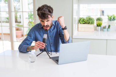 Mikrofon ve laptop kullanarak genç adam kayıt podcast rahatsız ve sinirle bağırarak sinirli, deli ve yükseltilmiş el, öfke kavramı ile bağırarak