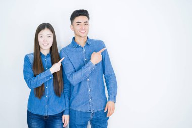 Yüzünde büyük bir gülümseme ile beyaz izole arka plan üzerinde güzel genç Asya çift, kamera bakarak yan el ve parmak ile işaret.