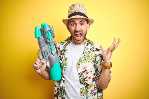 Junger Mann Hawaiihemd Mit Wasserpistole Vor Gelbem Hintergrund Sehr Glücklich — Stockfoto