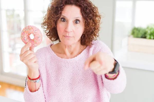 老女人吃粉红色的糖甜甜圈用手指指着相机和你 手符号 积极和自信的姿态从前面 — 图库照片