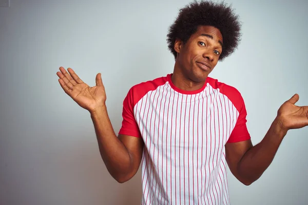 非洲裔美国男子 一个非洲头发 穿着红色条纹T恤在孤立的白色背景无知和混乱的表情与手臂和手抬起 怀疑概念 — 图库照片