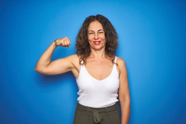 Mavi izole arka plan üzerinde ayakta kıvırcık saçlı orta yaş kıdemli kadın güçlü kişi gösteren kol kas, emin ve güç gurur