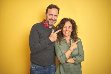 Yüzünde mutlu ve doğal ifade ile yan kadar el ve parmak ile işaret yüz bir gülümseme ile izole sarı arka plan neşeli üzerinde güzel orta yaş çift