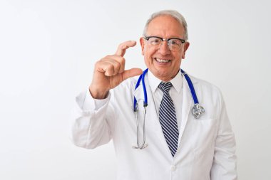 Üst düzey gri saçlı doktor adam izole beyaz arka plan üzerinde duran stetoskop giyen gülümseyerek ve emin el parmakları görünümlü ve kamera ile küçük boyutlu işareti yapıyor gesturing. Ölçü kavramı.