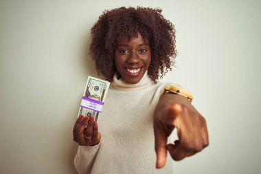 Genç afrikalı afro kadın kamera ve size parmak ile işaret izole beyaz arka plan üzerinde duran dolar tutan, el işareti, önden olumlu ve kendinden emin jest