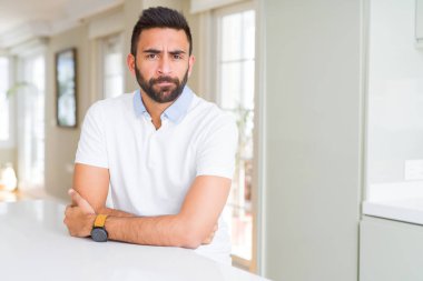 Yakışıklı İspanyol ev şüpheci ve sinir, onaylamayan ifade yüz çapraz kolları üzerinde rahat beyaz t-shirt dostum. Negatif kişi.