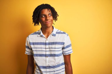 Zencili sarı arka plan üzerine çizgili gömlek giyen dreadlocks ile Afro Amerikan adam yan bakıyor ve düşünme uzağa bakıyor gülümseyen.