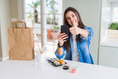 Güzel genç kadın büyük gülümseme ile akıllı telefon kullanarak uygulamadan gıda teslim sipariş ok işareti yapıyor, parmaklar ile başparmak, mükemmel işareti