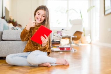 Güzel genç kız çocuk dijital Touchpad tablet kullanarak katta oturan mutlu büyük gülümseme ile ok işareti, başparmak yukarı parmaklar, mükemmel işareti yapıyor